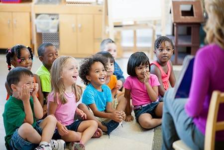 Children seated as preschool teacher reads book