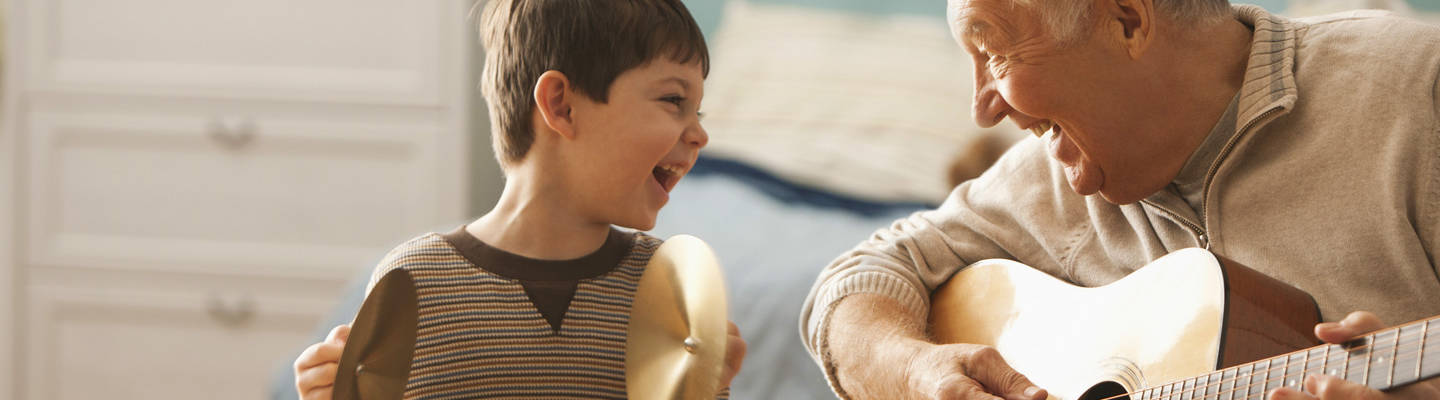 Grandfather playing guitar with young boy with cymbals