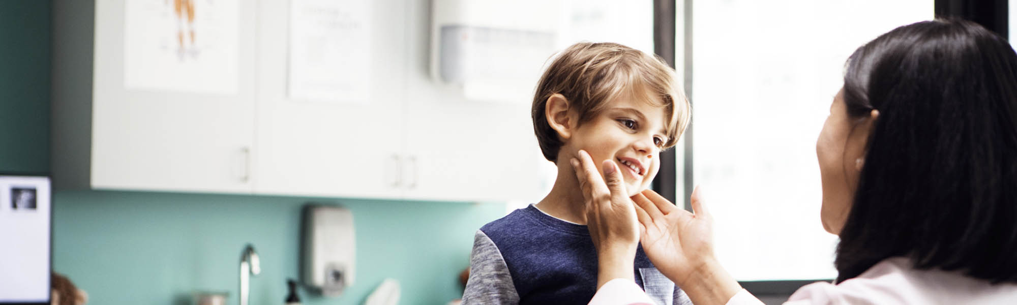 pediatrician touches neck of young boy in clinic