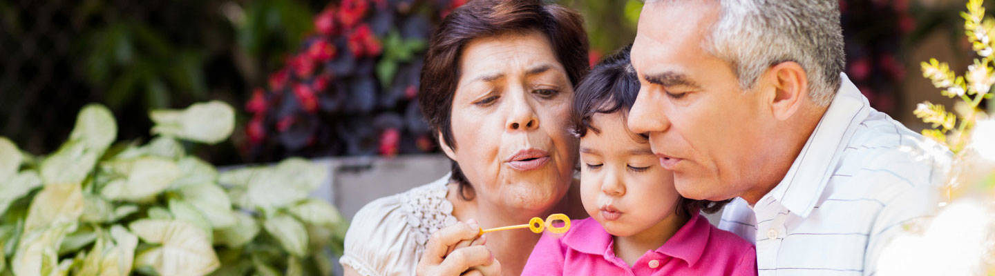 Grandparents blowing bubbles outside with their grandchild.
